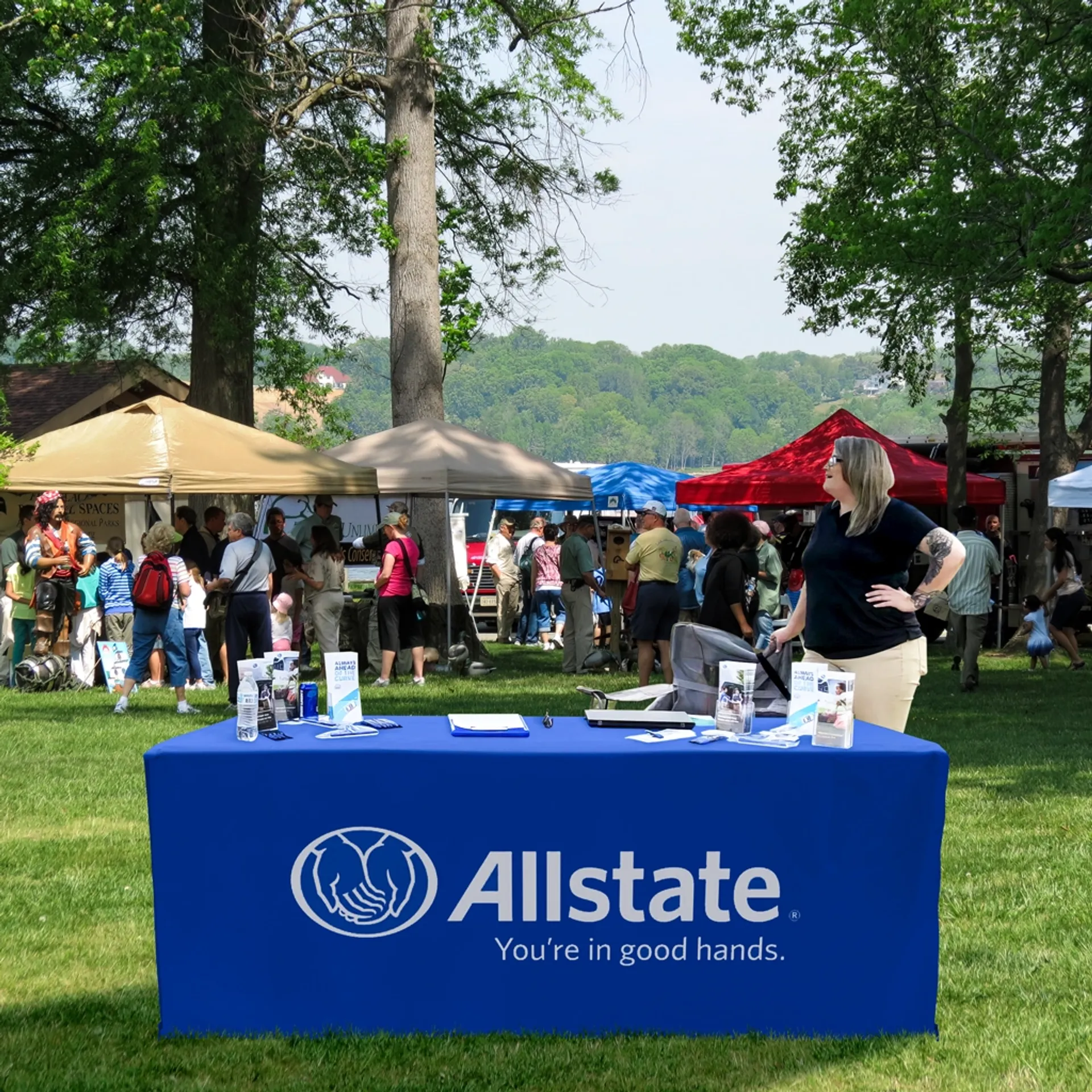 Outdoor event scene with a 6ft fitted table cover in royal blue, shown as a customizable display table setup for promotional use.