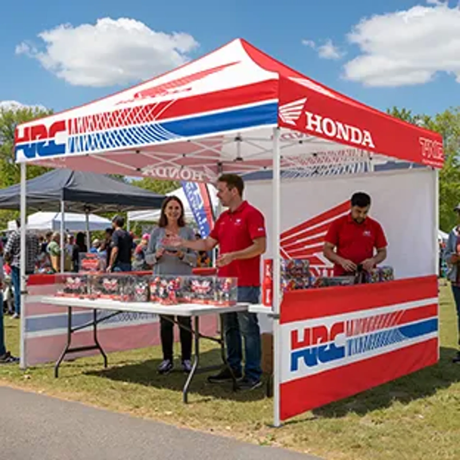 A branded custom pop-up tent featuring red, white, and blue Honda and HRC logos at an outdoor event, with staff standing behind a display table under the promotional event canopy.