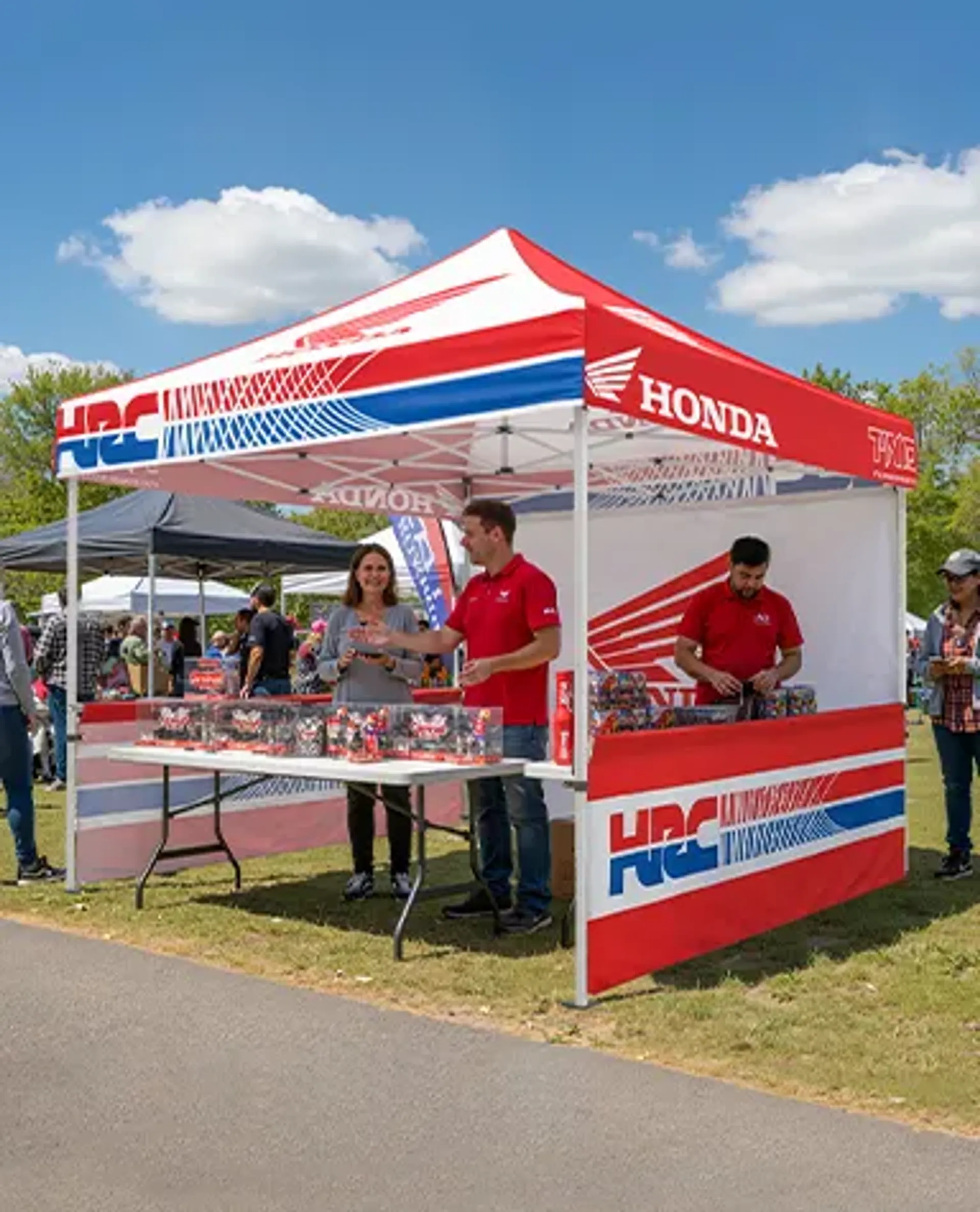 A branded custom pop-up tent featuring red, white, and blue Honda and HRC logos at an outdoor event, with staff standing behind a display table under the promotional event canopy.