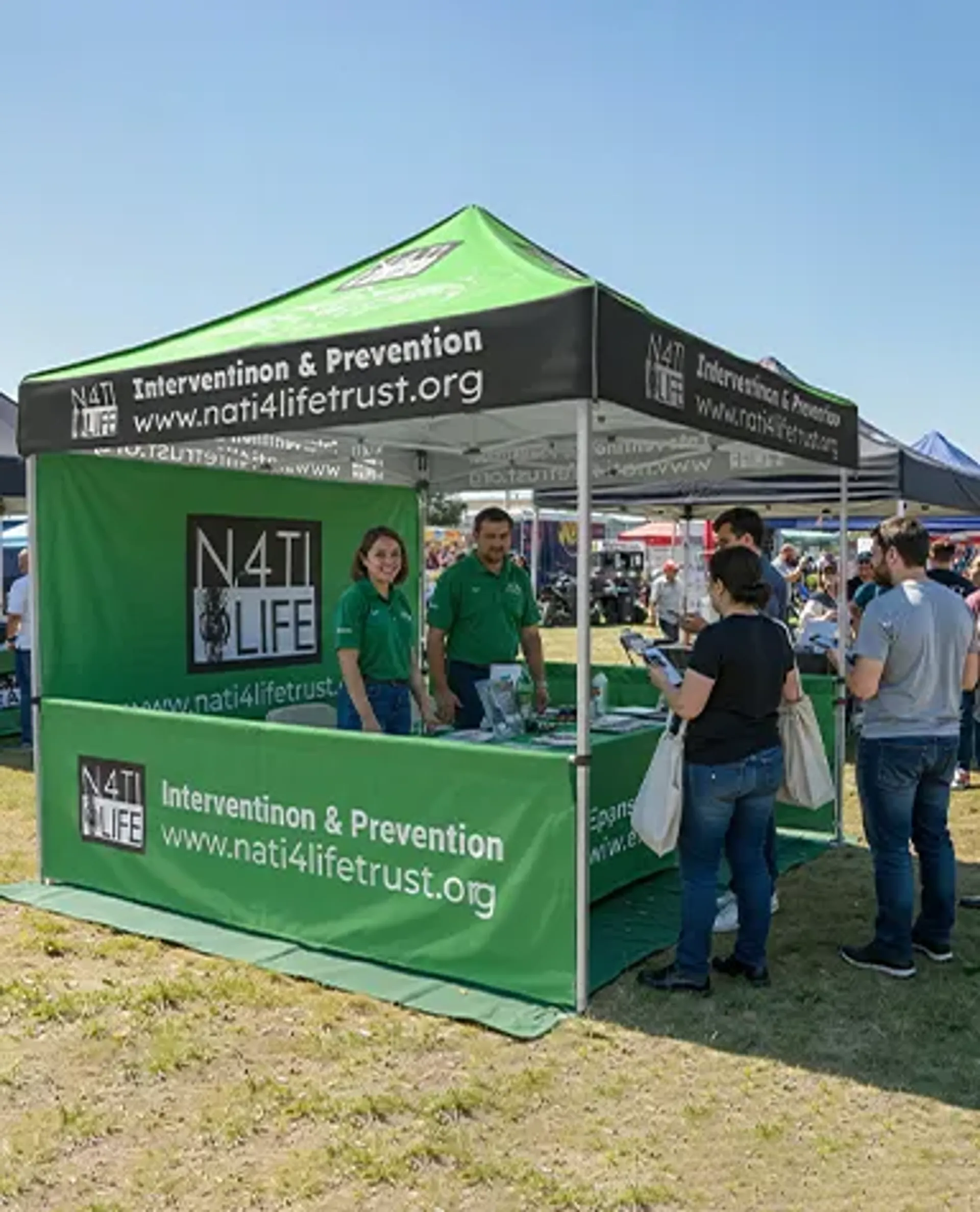 A green and black custom printed event tent for "N4TI 4 LIFE" featuring branded half walls and canopy roof, functioning as an outdoor informational pop-up booth where staff speak with visitors.