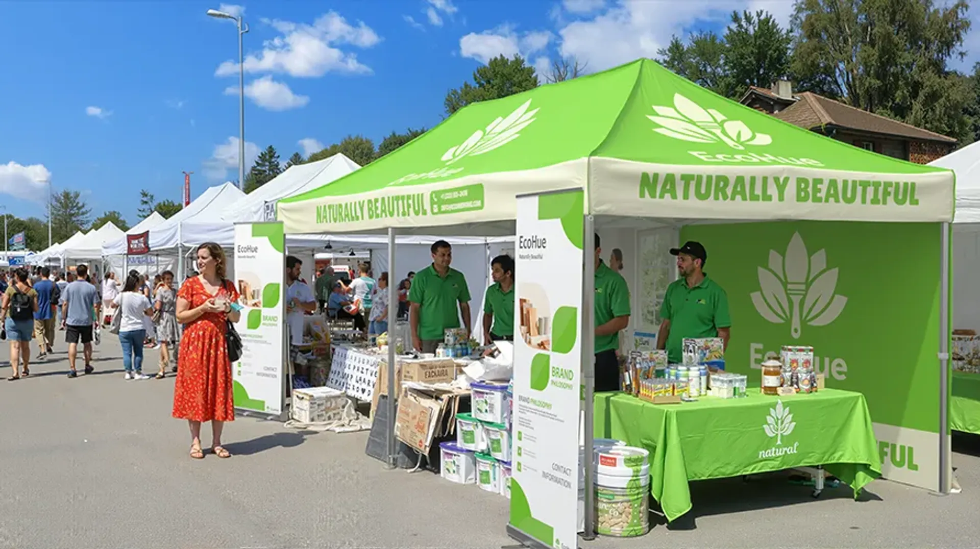 A custom printed green event canopy for the brand "EcoHue" at a sunny outdoor festival, showcasing natural products on a display table to eventgoers.