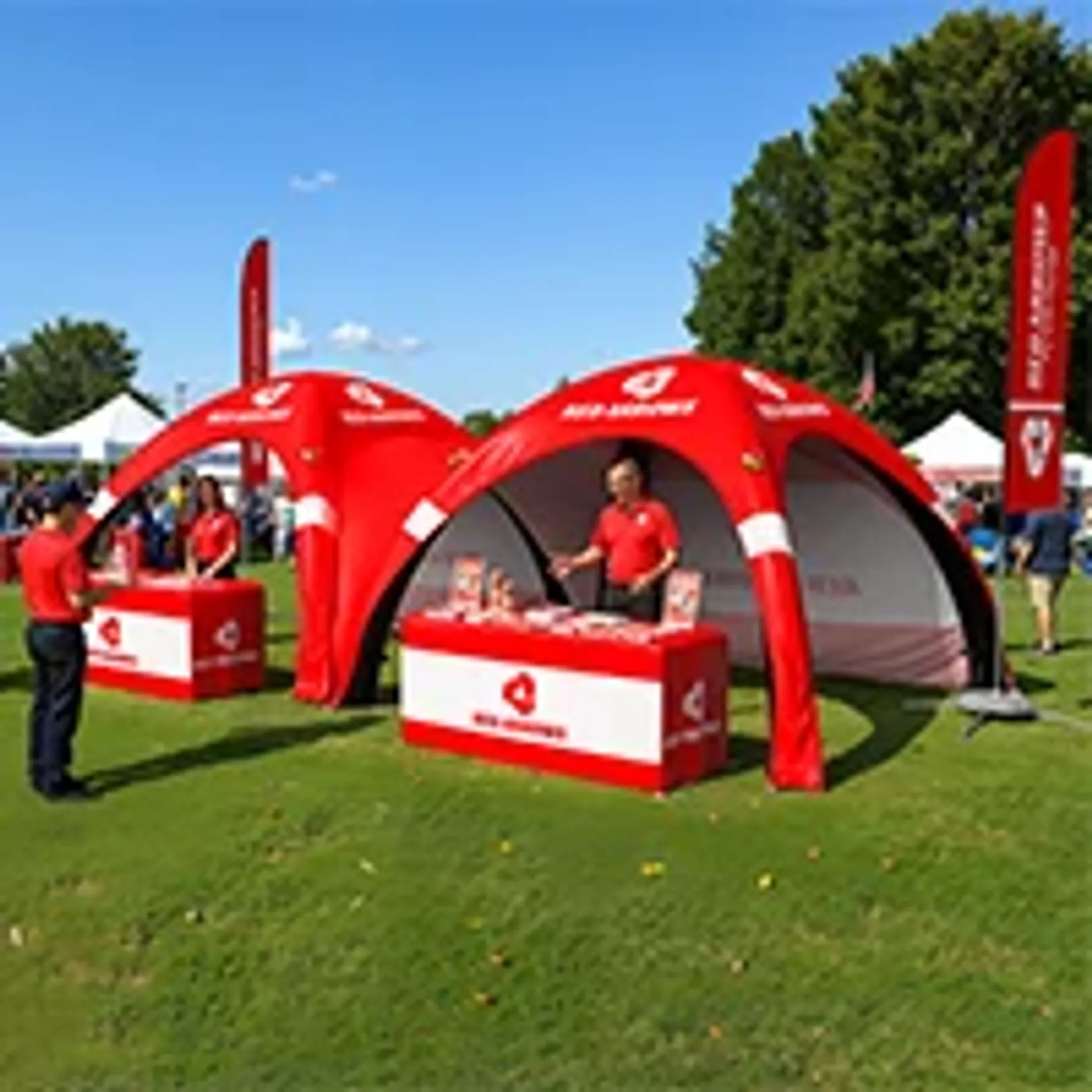 Matching red custom inflatable event tents used as outdoor promotional booths with branded table covers and flags