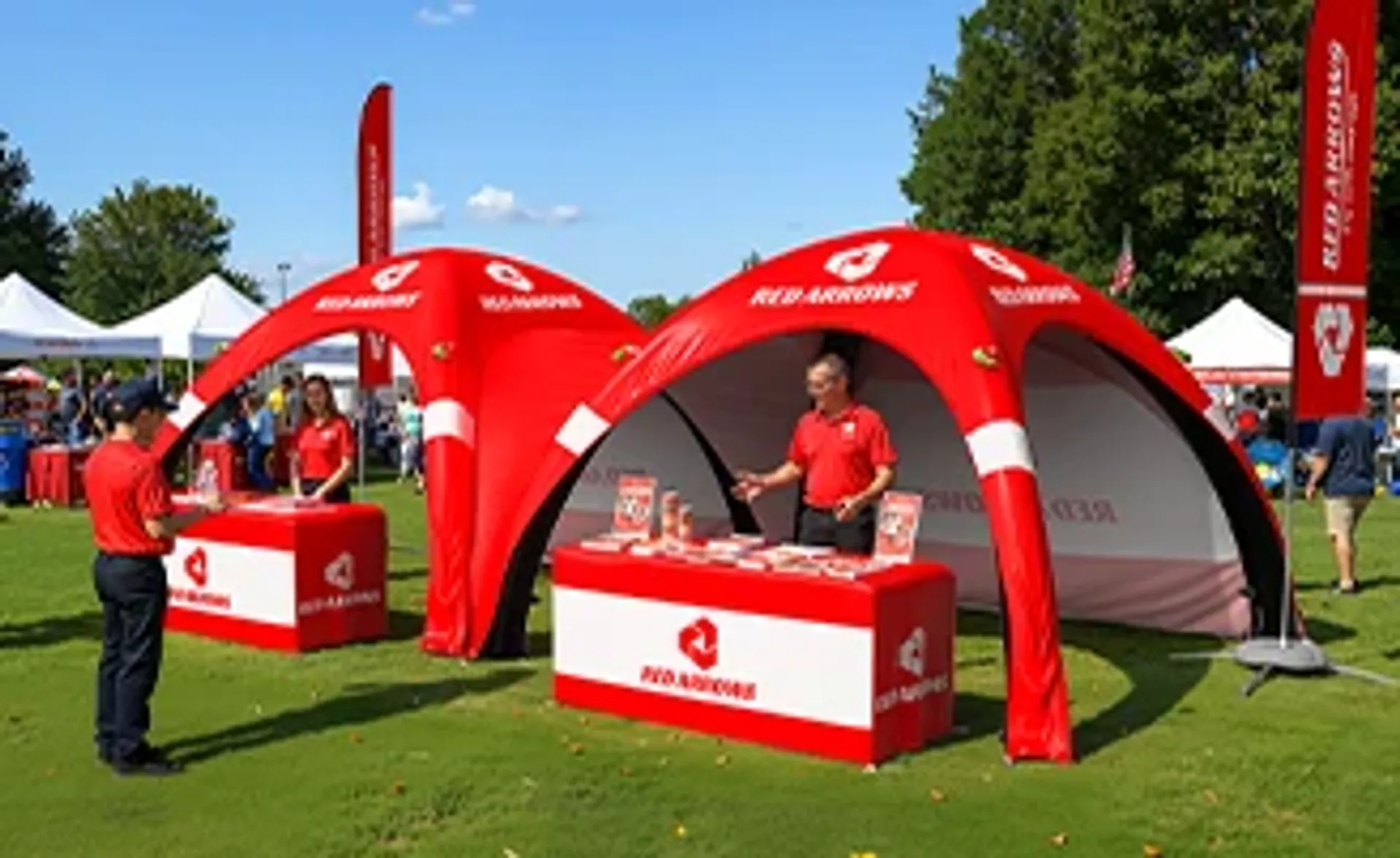 Matching red custom inflatable event tents used as outdoor promotional booths with branded table covers and flags