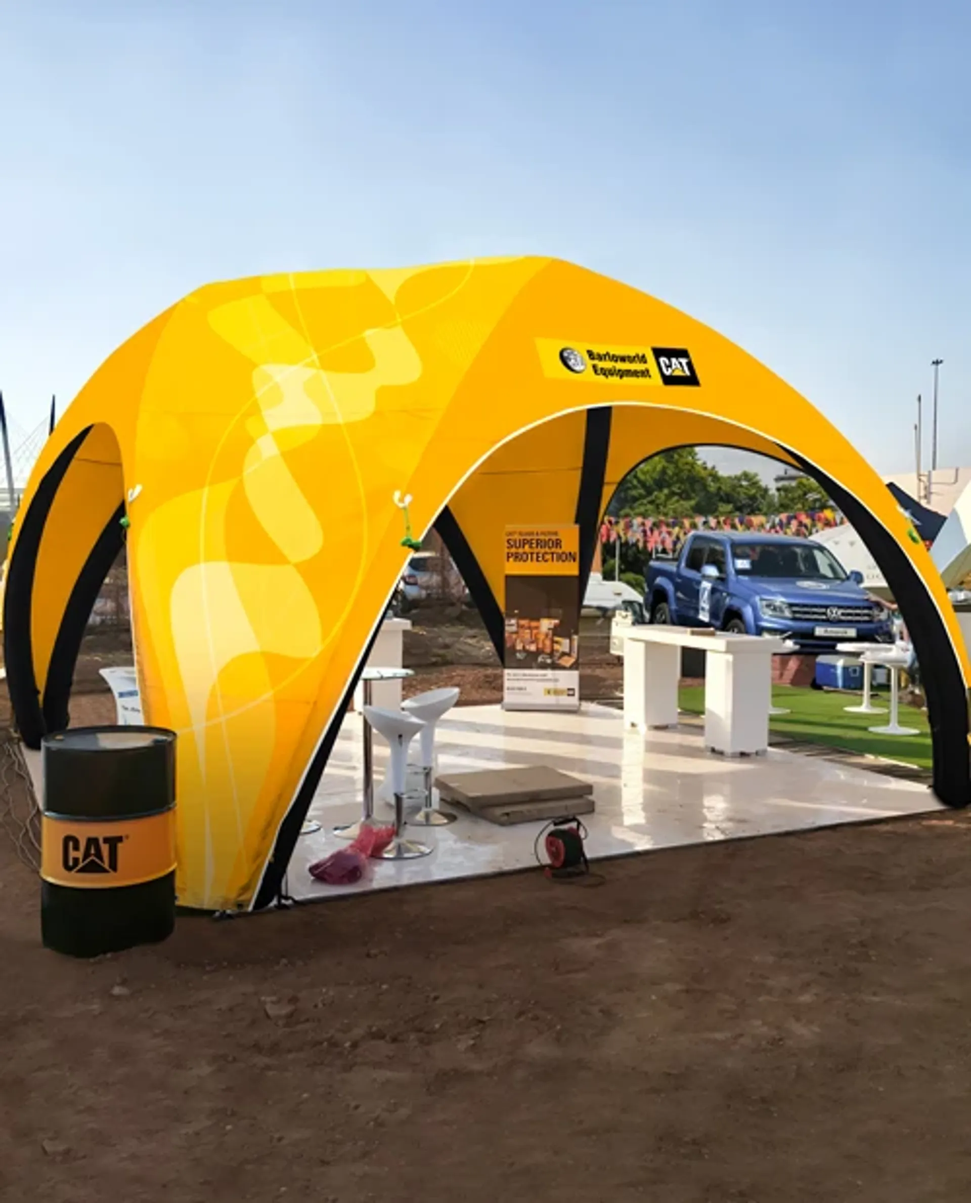 Yellow custom inflatable dome tent with corporate branding used as an outdoor industrial equipment showcase booth on a dirt lot