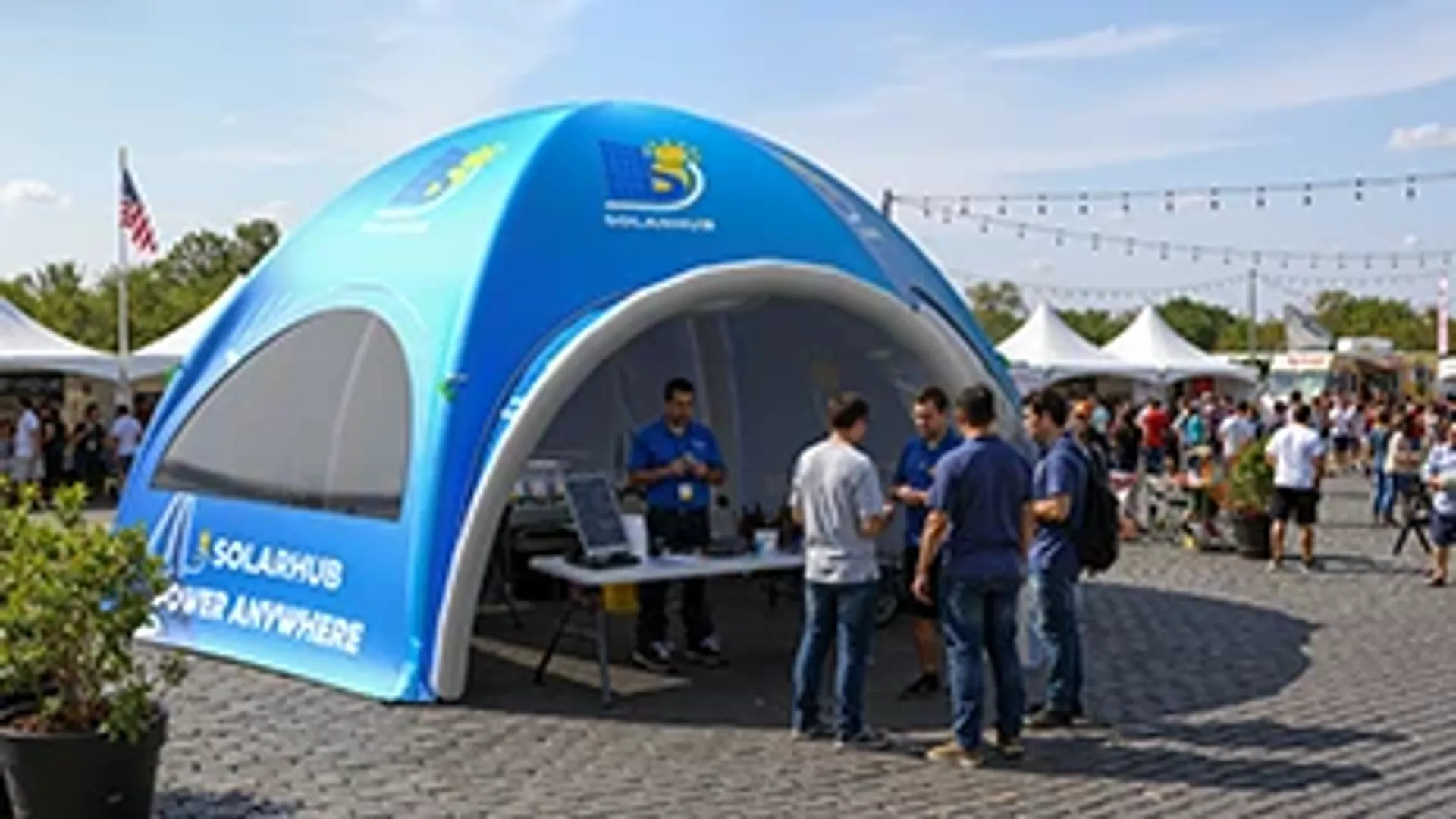Blue custom inflatable promotional dome tent used as a brand activation booth for a tech company at a sunny outdoor festival