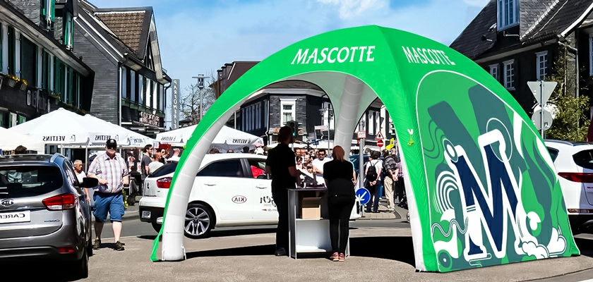 A green custom printed inflatable tent with a full wall on one side stands at the market