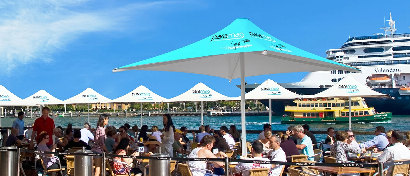 A row of heavy-duty market umbrellas stands at the river's edge, providing volume for riverside tables. These oversized umbrellas make a beautiful sight along the riverfront