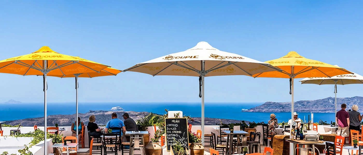 At the cafe by the sea, three custom market umbrella with pulley system were placed by the tables and chairs. People enjoying the afternoon under the patio umbrellas